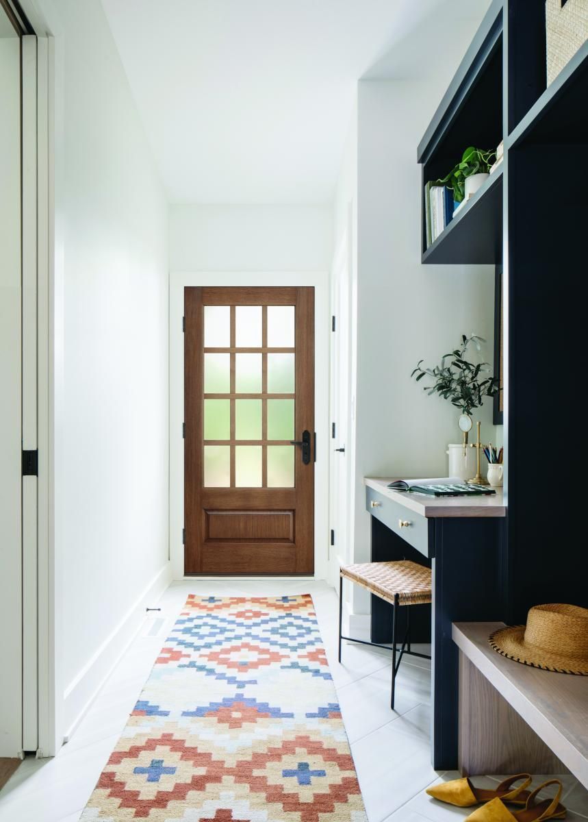 Narrow entry hallway with a patterned runner rug, wooden door, and dark built-in shelves and desk.