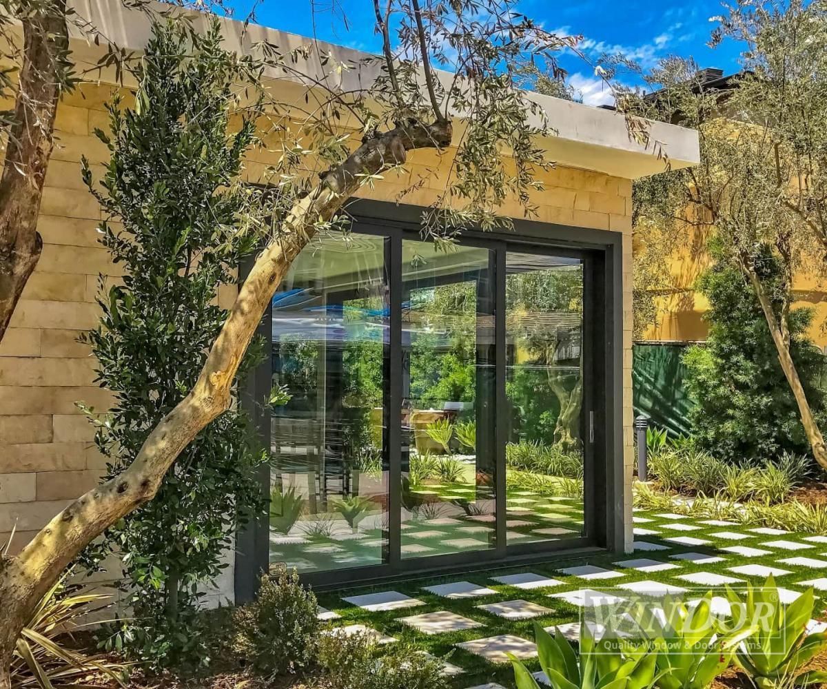 Modern glass patio doors under a vine-covered pergola in a sunlit garden courtyard