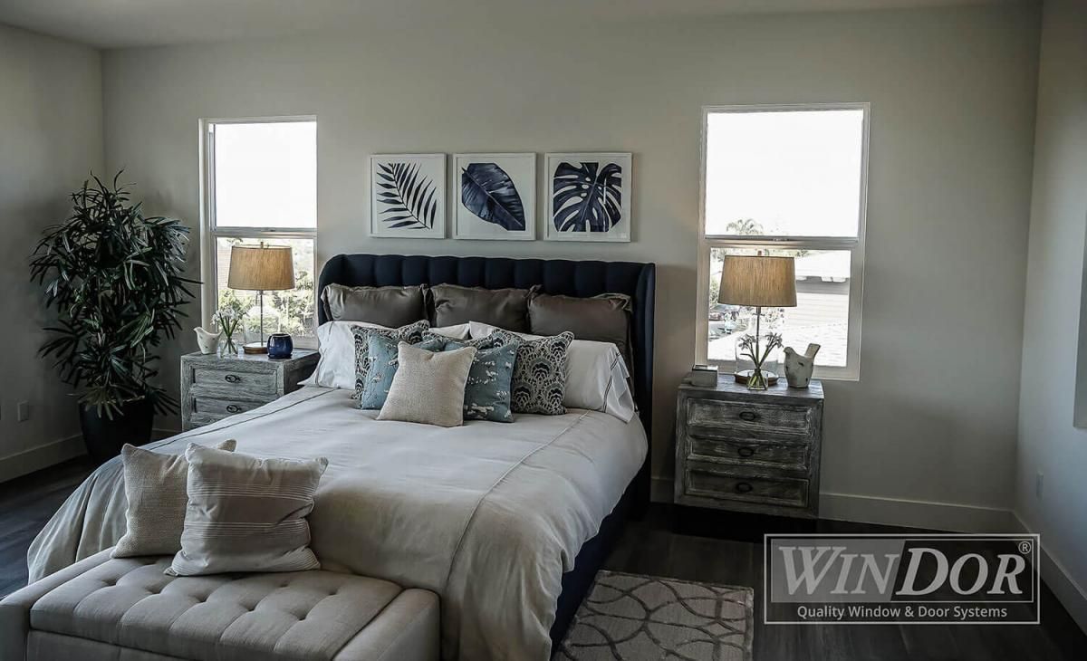 Cozy bedroom with a tufted bed, two windows, bedside lamps, and framed wall art
