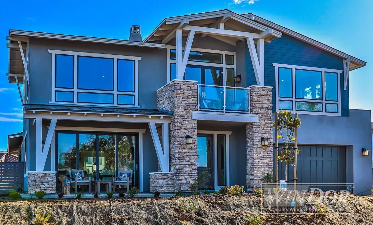 Modern two-story house exterior with stone accents, large windows, and a balcony under construction.