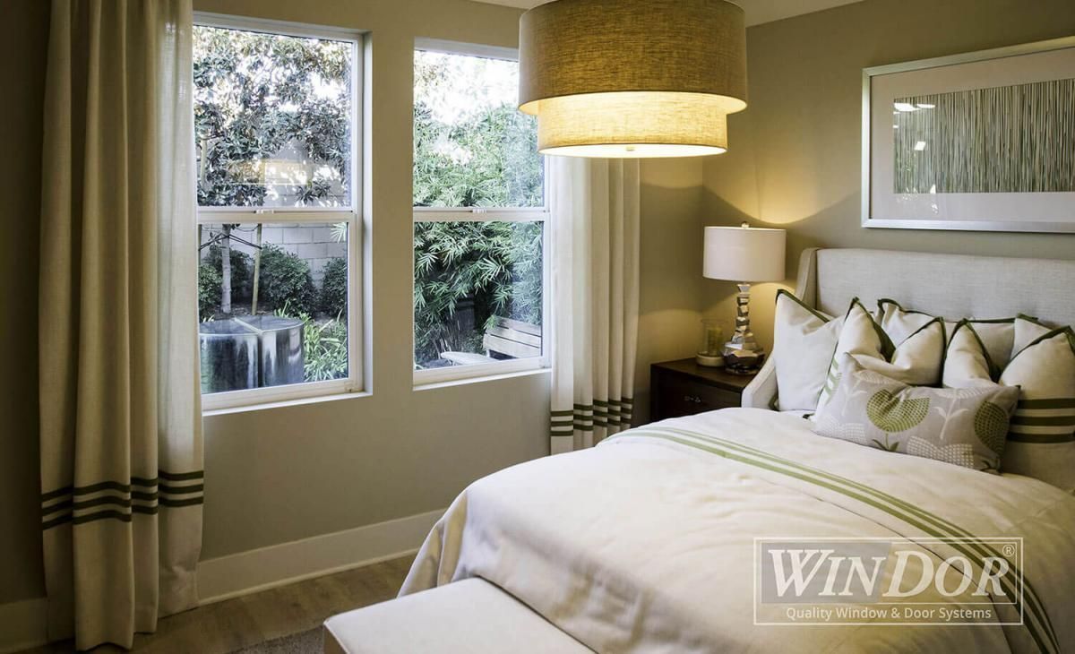 Bright bedroom with a bed, bedside lamp, woven pendant light, and windows showing trees outside