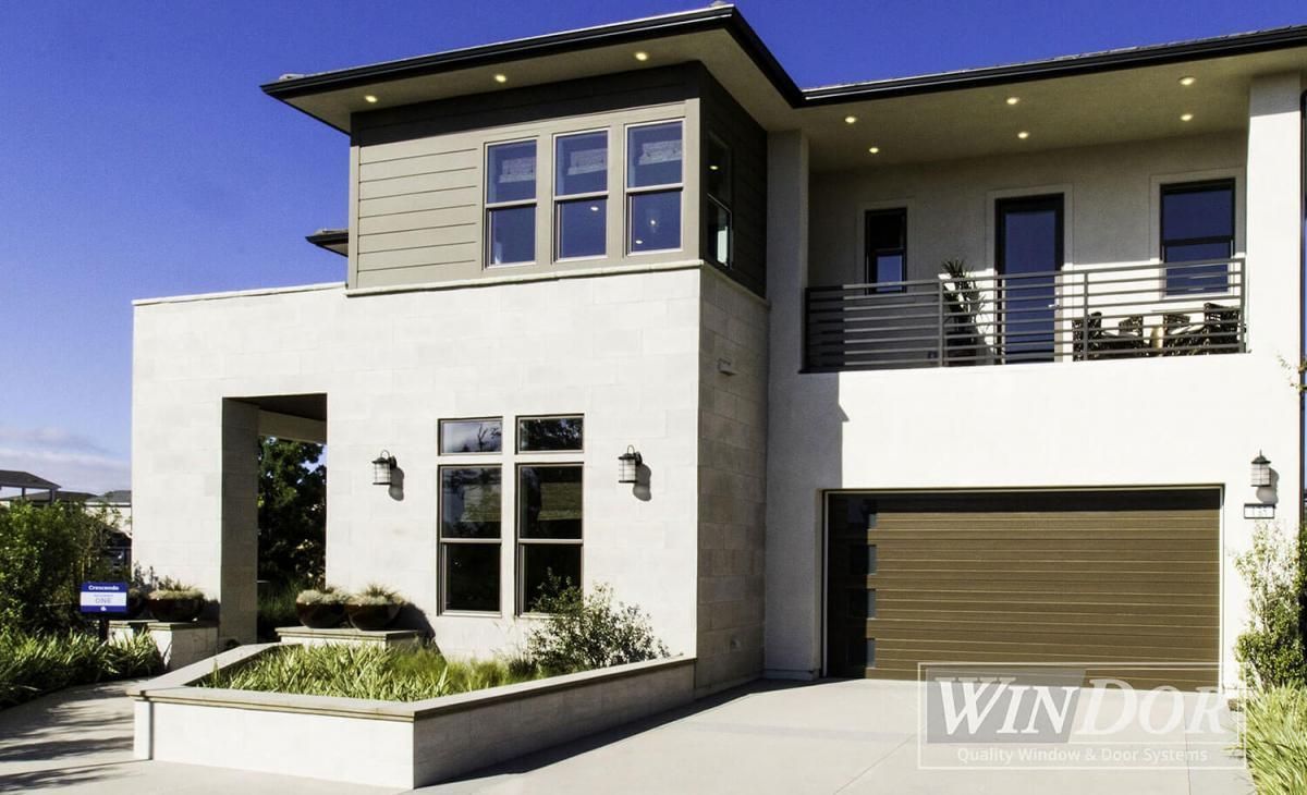 Modern two-story white house with garage, balcony, and landscaped front entry under a blue sky