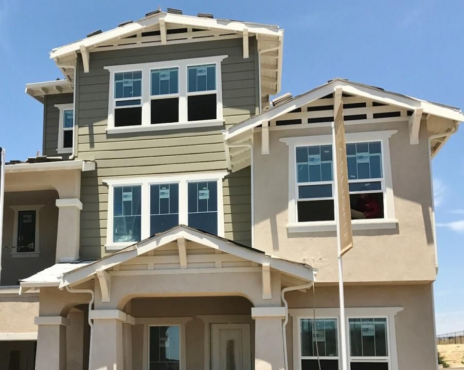 Two-story beige and gray house exterior with white trim and multiple windows under a blue sky