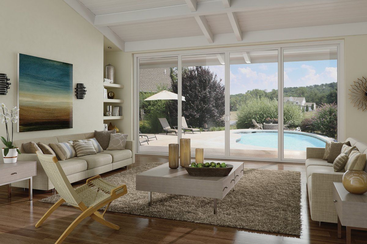 Bright living room with white sofas, a shag rug, and large windows overlooking a pool and garden.
