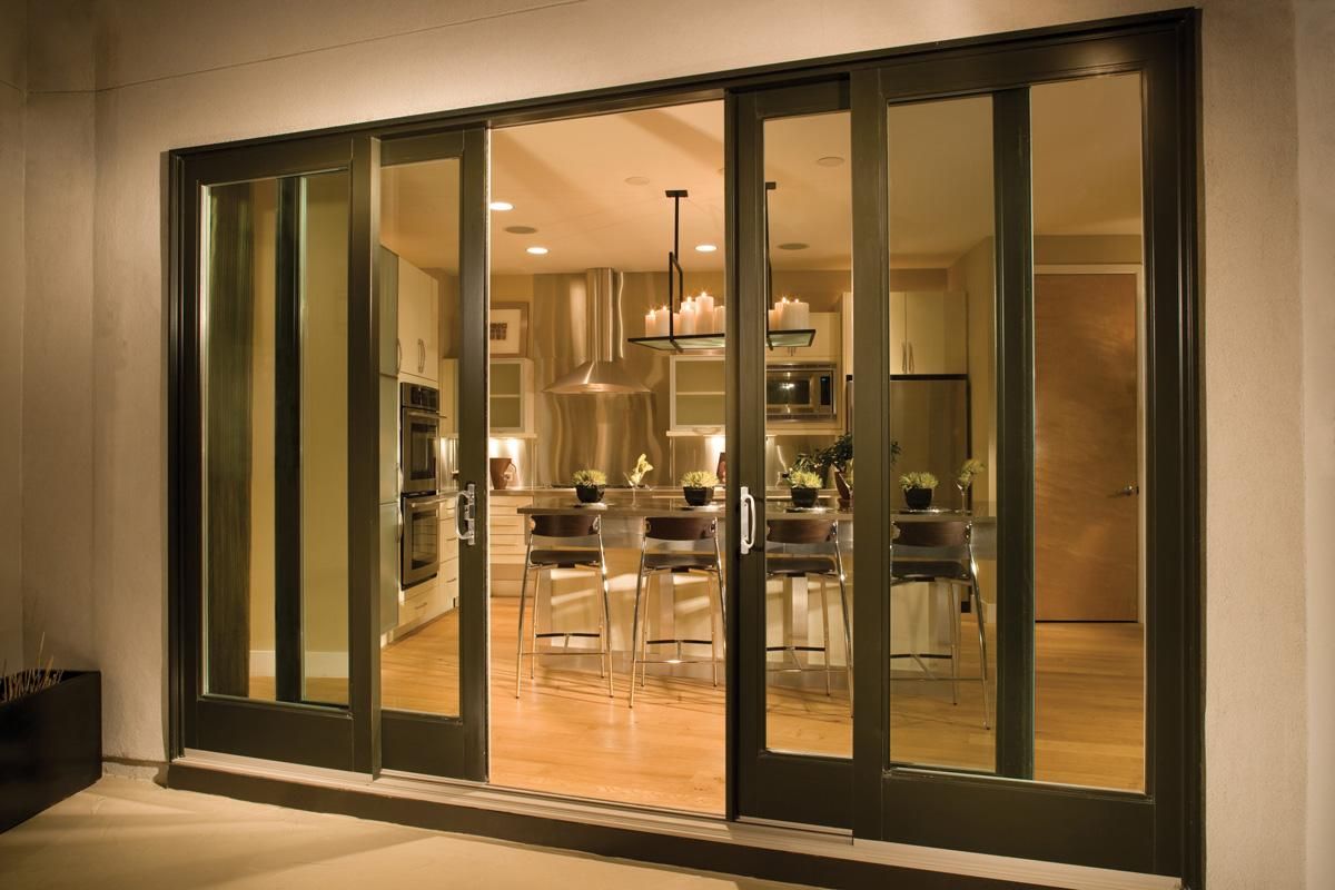 Glass sliding doors reveal a warm, modern kitchen and dining area inside a contemporary home