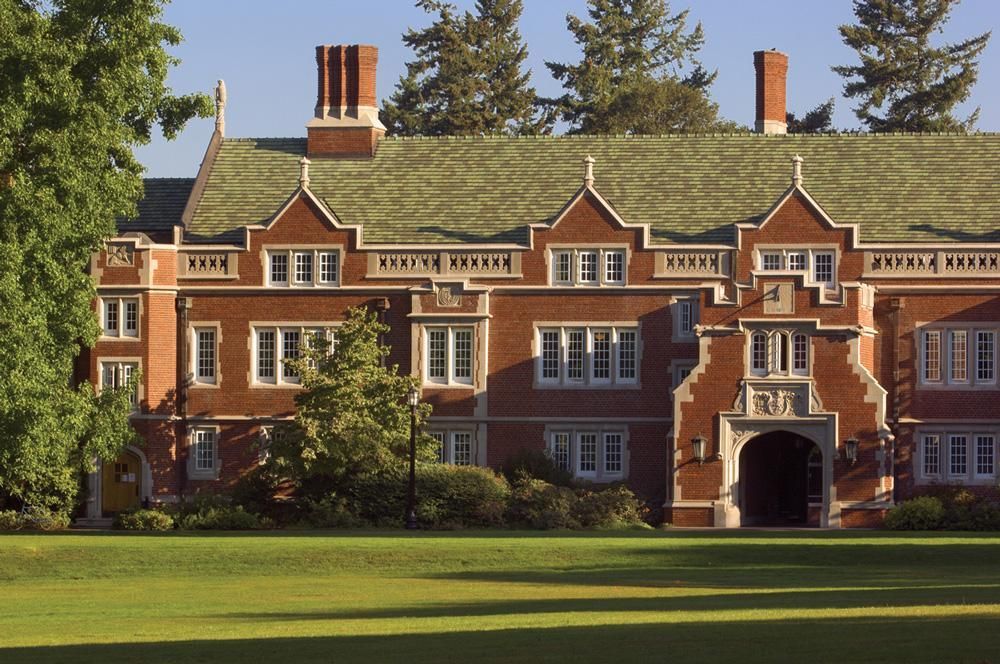 Red-brick manor house with ivy roof, chimneys, and arched entrance in a green lawn setting