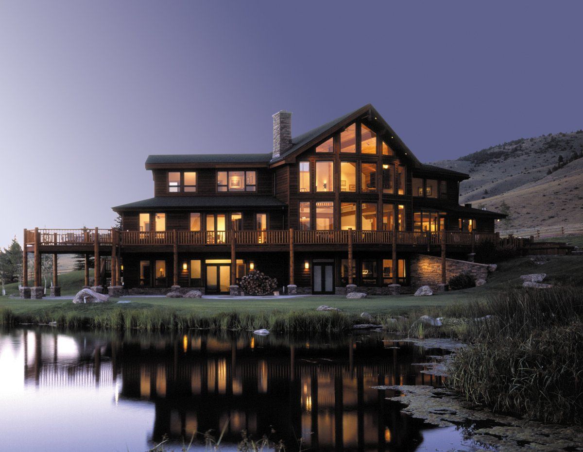 Lit log cabin lodge by a lake at dusk, with warm window lights reflected in the water.