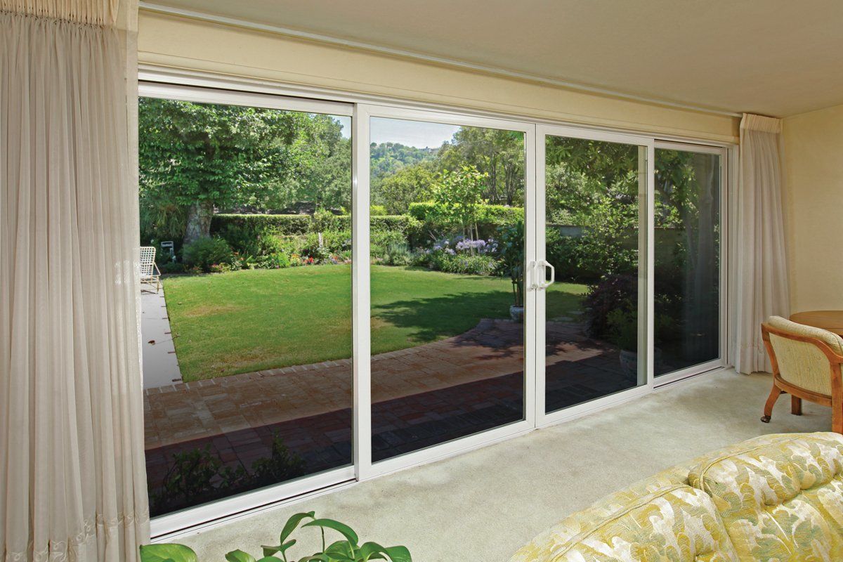 Sliding glass doors open to a green backyard, with beige curtains and a glimpse of a bed inside.