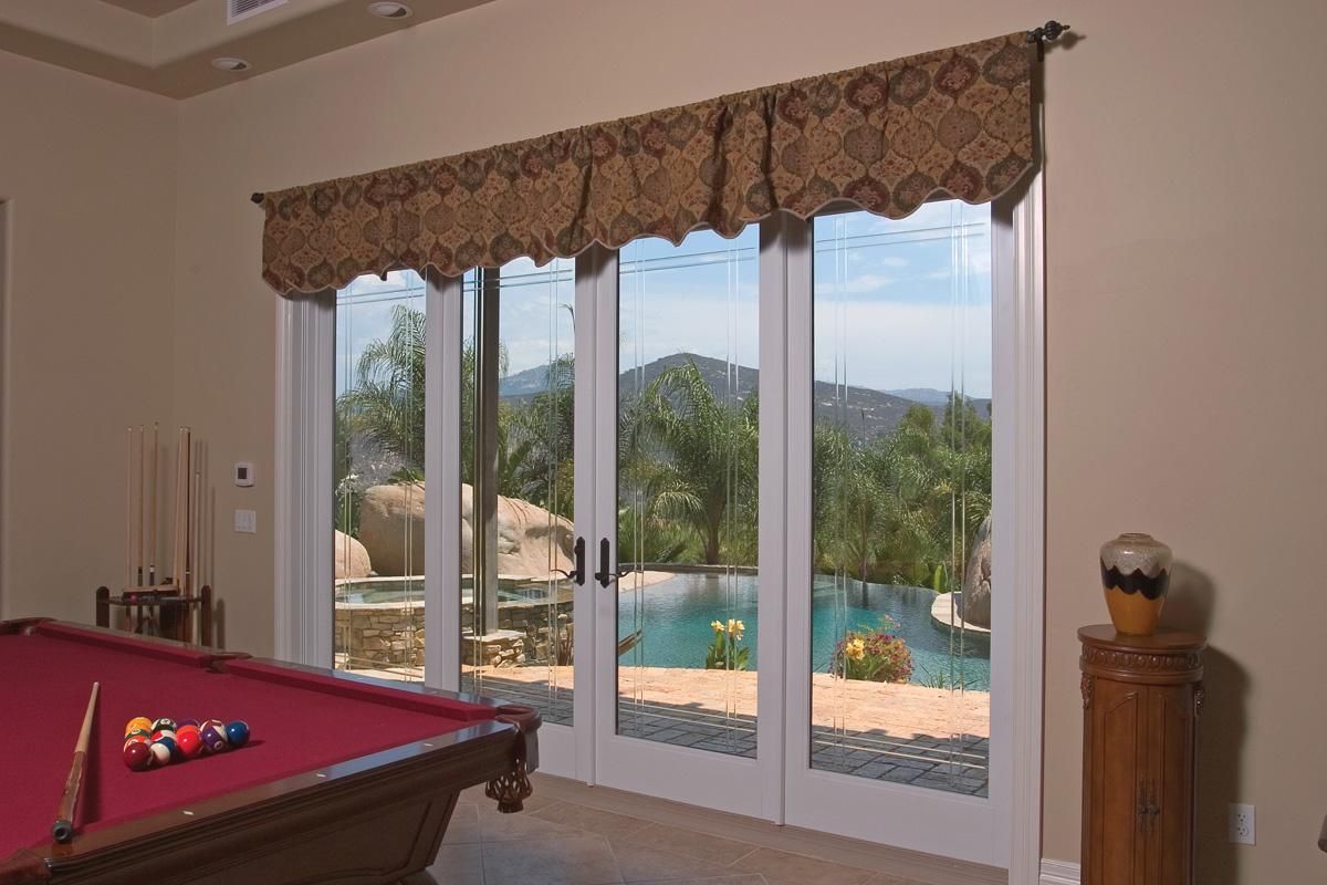 Poolside view through patio doors from a room with a pool table and draped valance
