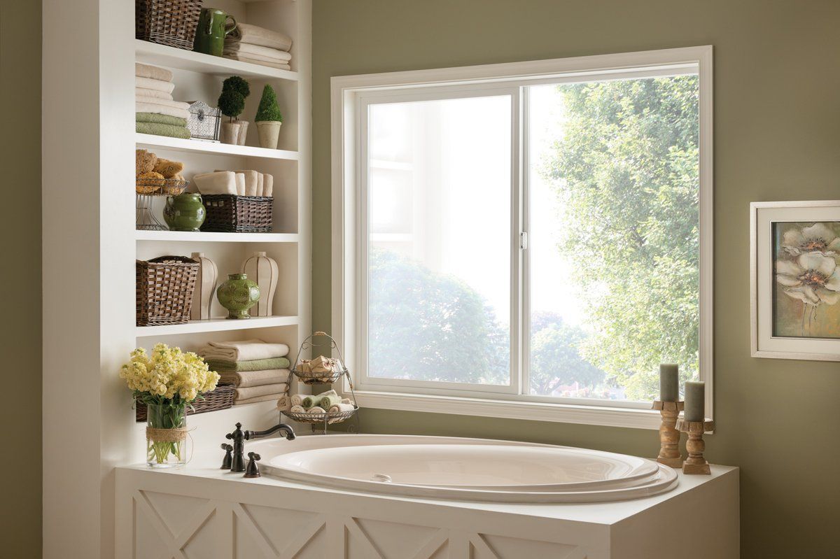 Bright bathroom with a freestanding tub, window, shelves, and flowers in soft neutral tones