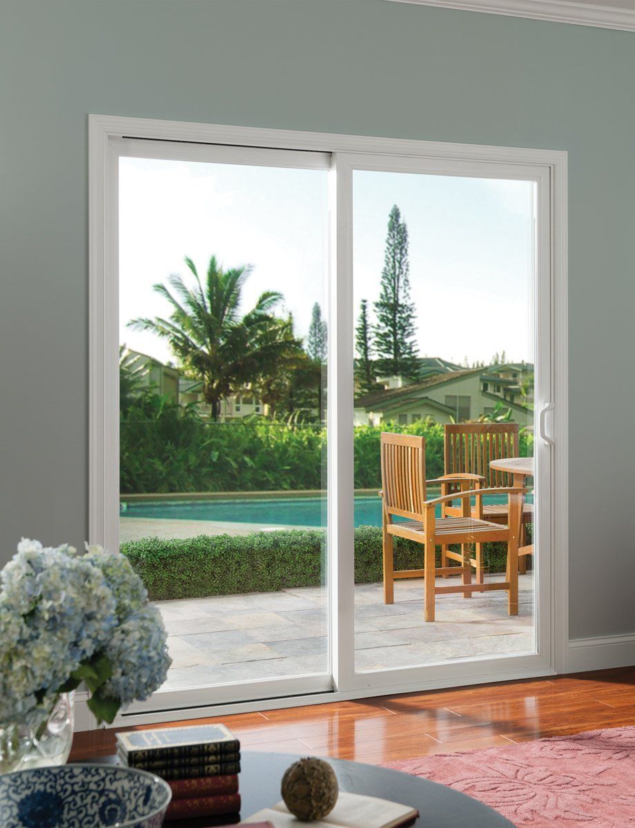 Sliding glass doors opening to a patio and garden with palm trees and wooden chairs