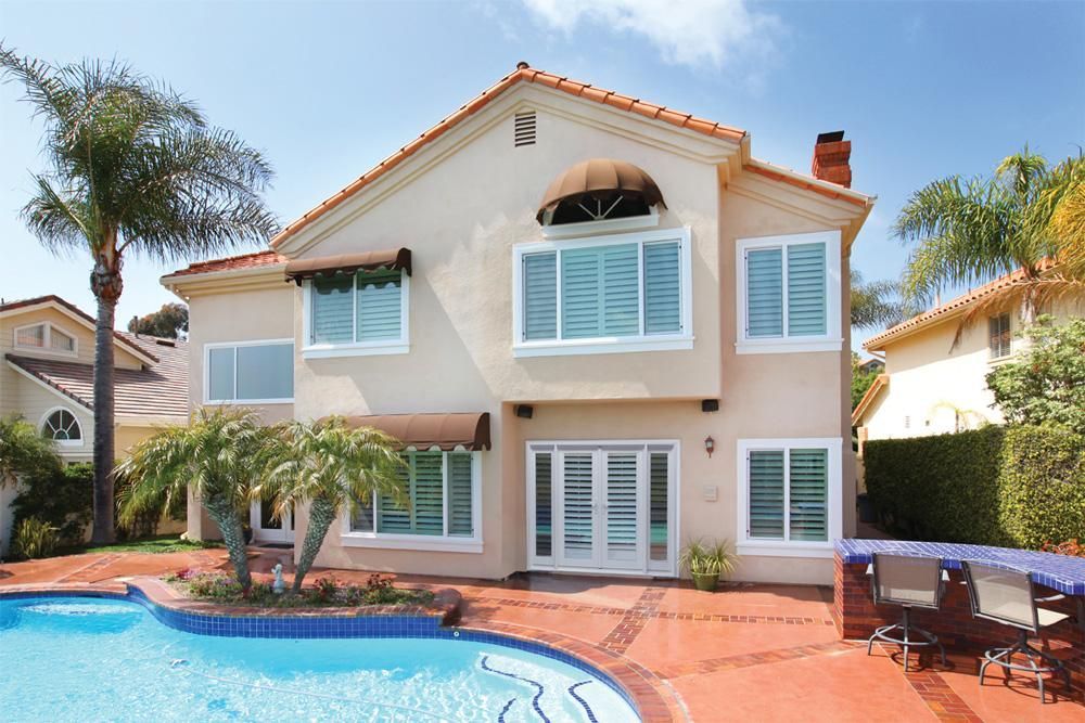 Two-story cream house with turquoise shutters beside a blue pool on a sunny day