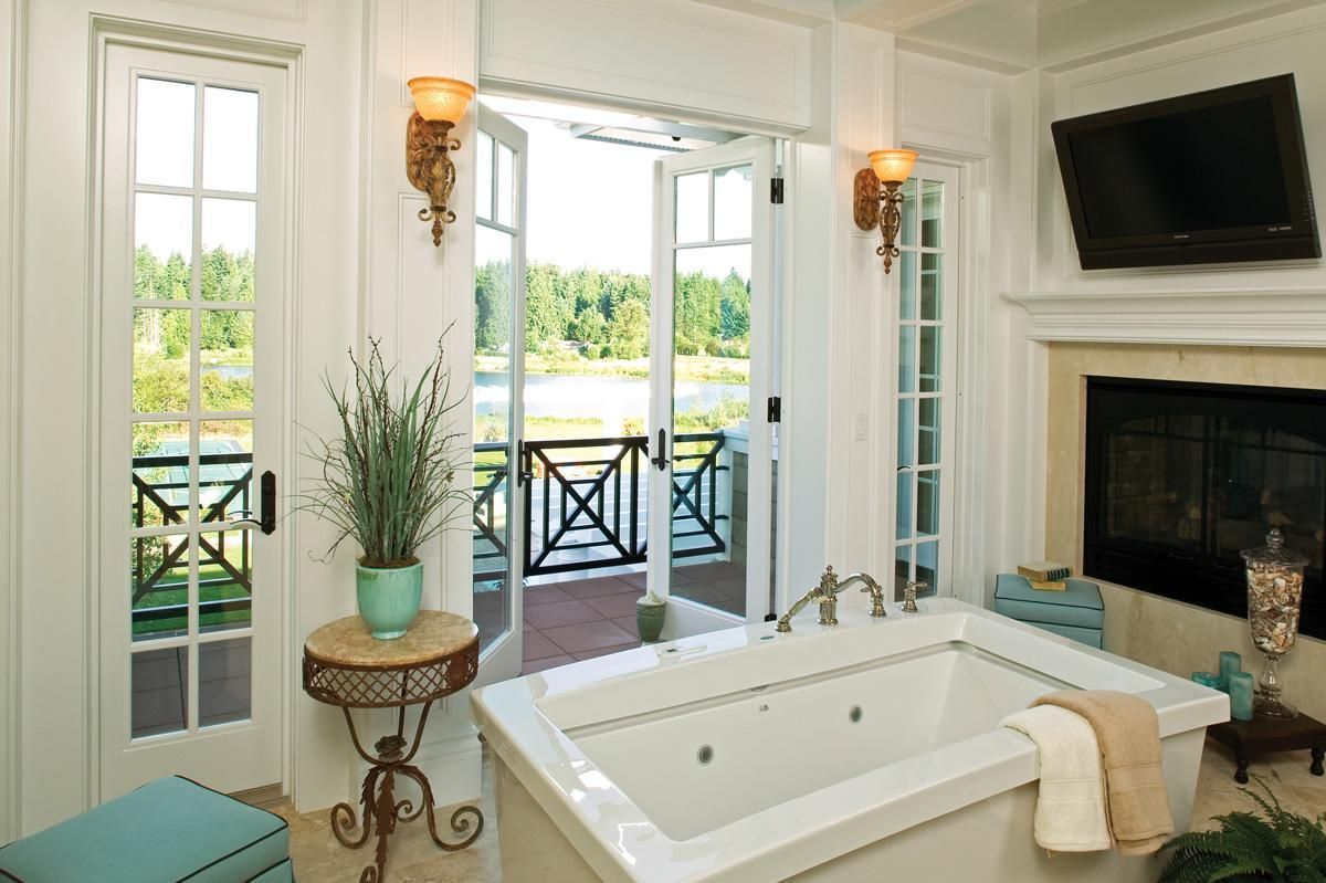 Bright bathroom with a soaking tub, fireplace, and open doors overlooking a waterfront balcony.