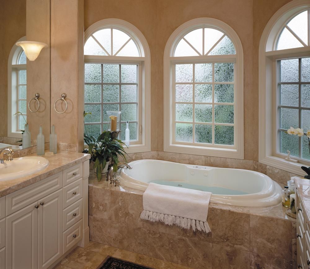 Elegant beige bathroom with arched windows, a soaking tub, and a vanity beside a frosted glass shower.