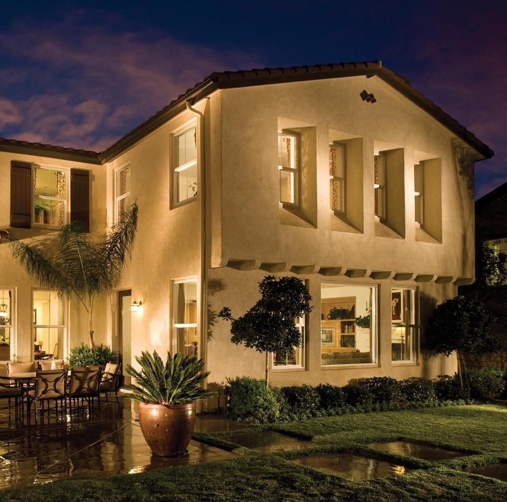 Warmly lit two-story stucco house at dusk with a landscaped yard and outdoor seating area