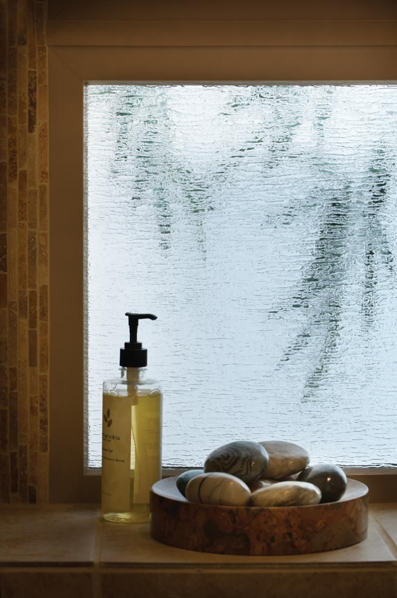 Soap dispenser and bowl of stones on a windowsill beside a frosted window