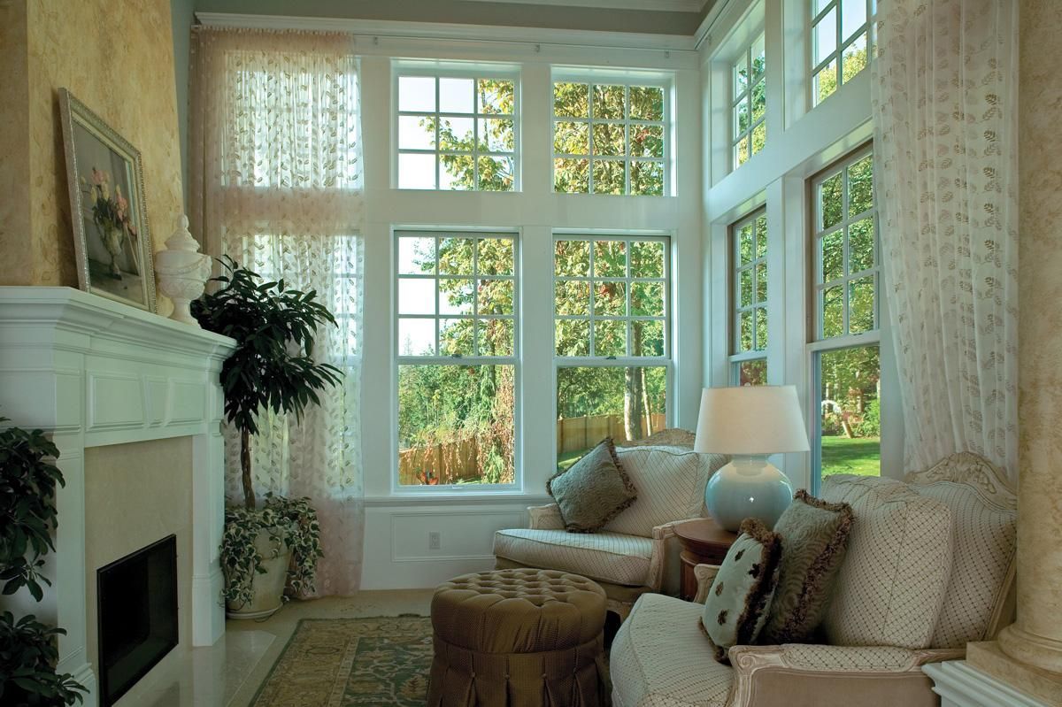 Bright sunroom with large windows, cream sofa, fireplace, and plants overlooking a leafy garden.