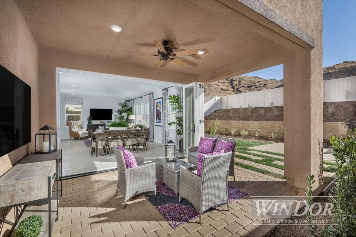 Covered patio with wicker seating and purple cushions opening to a bright indoor living area and backyard.