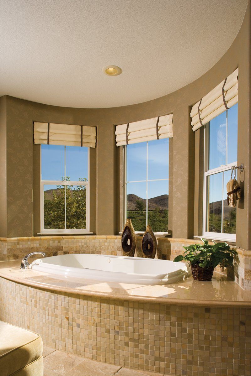 Bright bathroom with a curved soaking tub, tan tile, and large windows overlooking a sunny landscape