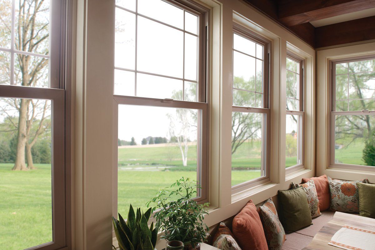 Sunroom with large windows overlooking a green lawn and trees, with cushioned seating by the window