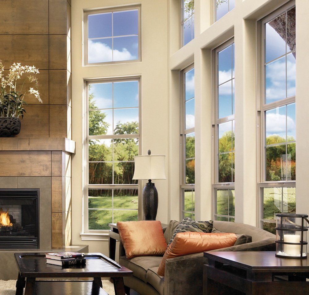 Bright living room with large windows, fireplace, tan sofa, and a view of the green yard outside