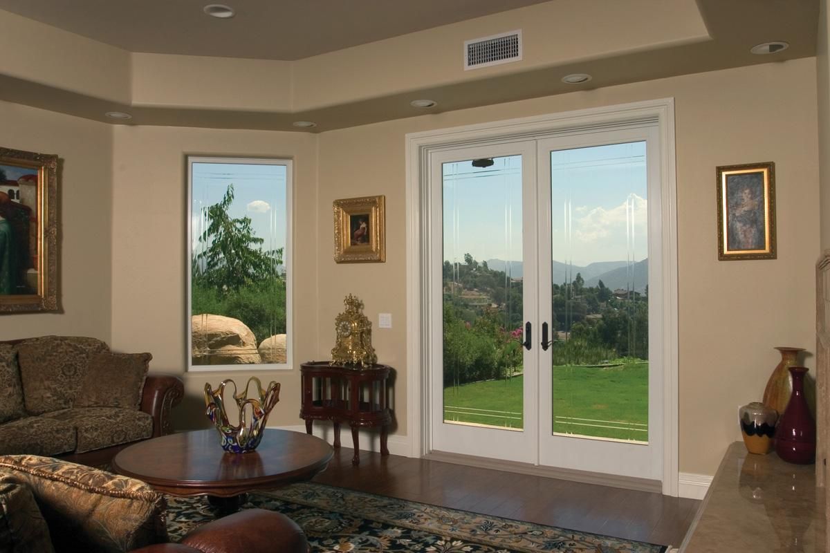 Cozy living room with sliding glass doors opening to a green garden and a window view of trees and hills.