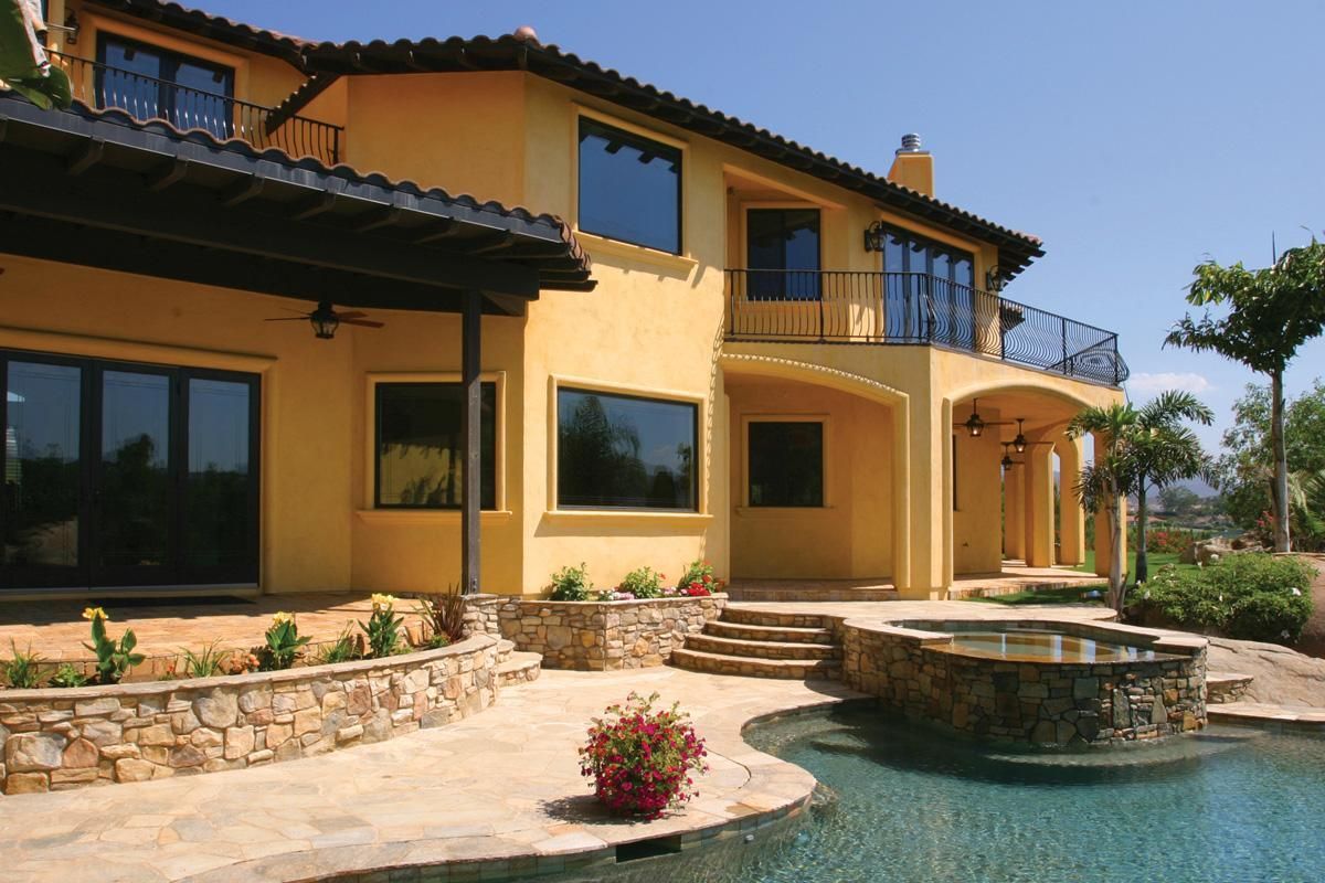 Luxury two-story yellow villa with stone patio and pool beside a landscaped yard