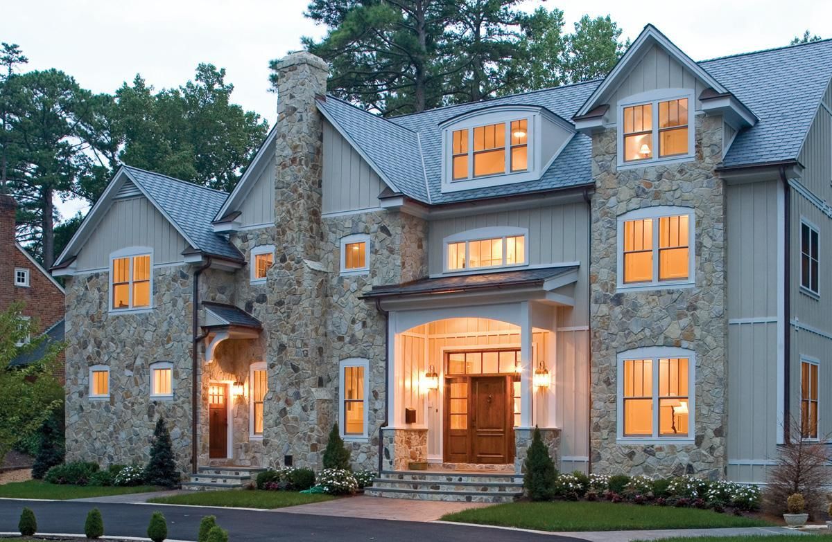 Large stone and stucco luxury house with lit windows and warm entrance lights at dusk