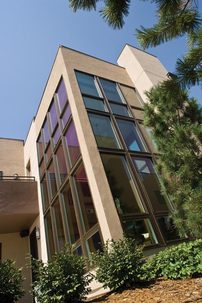 Modern building with tall glass windows, viewed from below against a blue sky and trees
