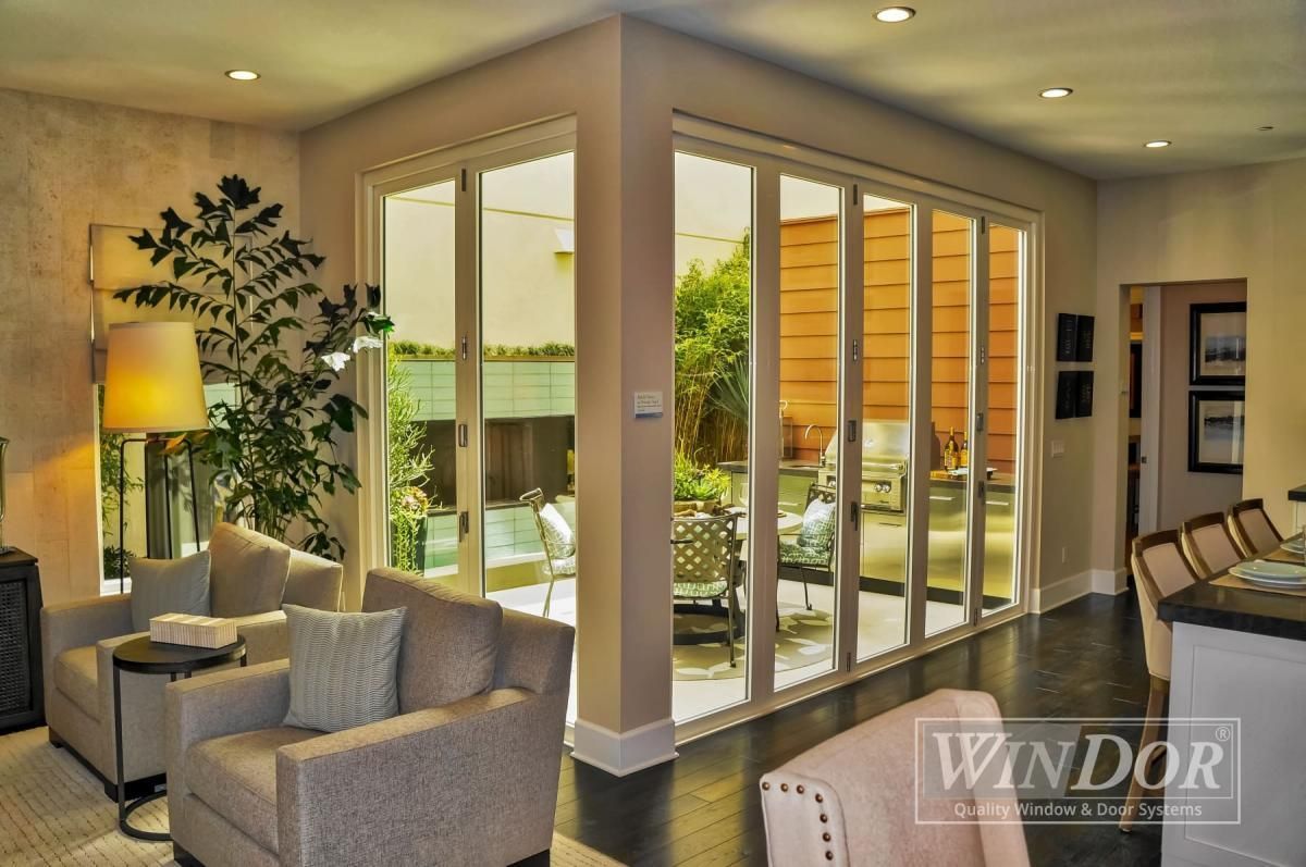 Modern living room with beige seating, potted plant, and large glass doors opening to a patio.