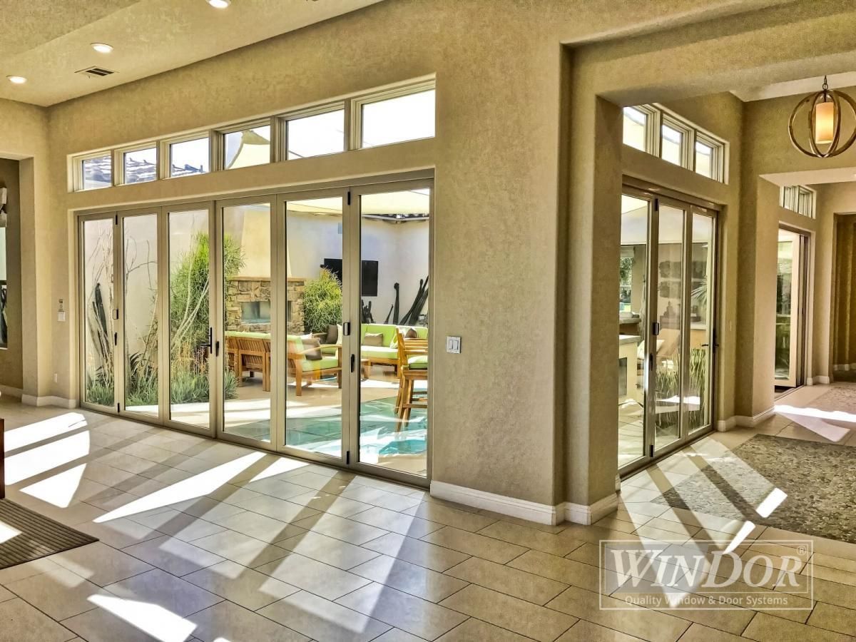 Sunlit empty living room with large windows, tiled floor, and view of a patio and pool