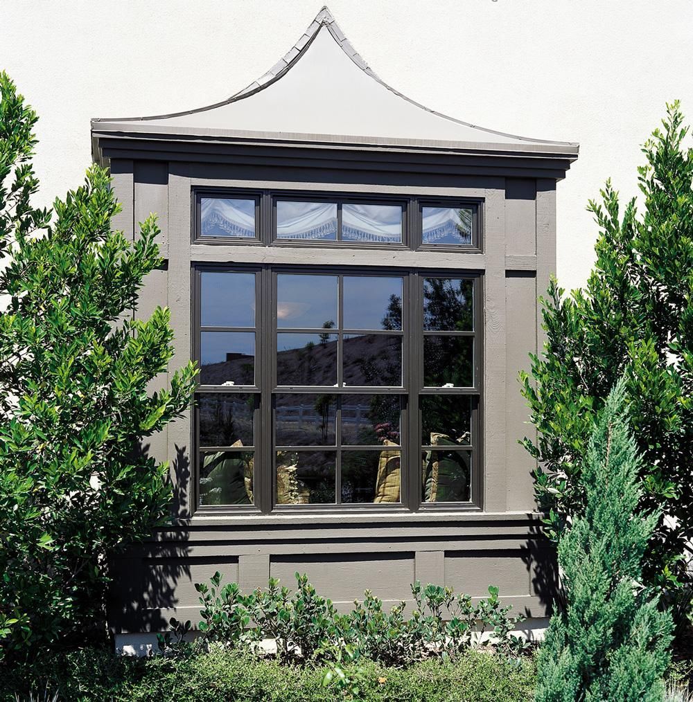 A stucco building facade with a large blue-paned window, framed by trees and shrubs.