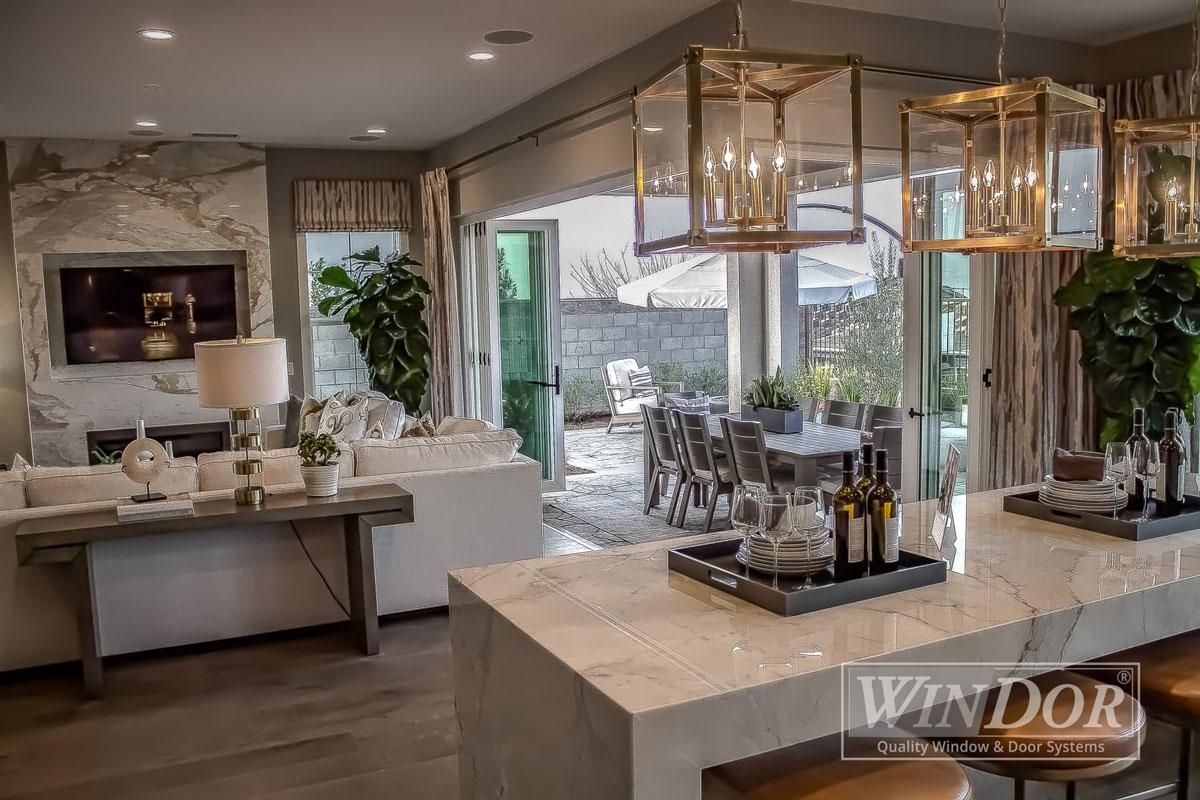 Modern luxury kitchen and dining area with marble island, pendant lights, and large windows overlooking a patio