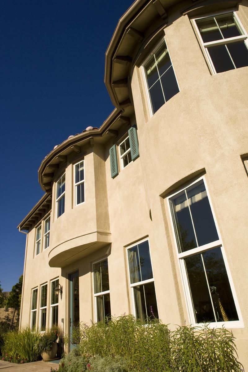 Curved beige stucco house exterior with tall windows and a blue sky