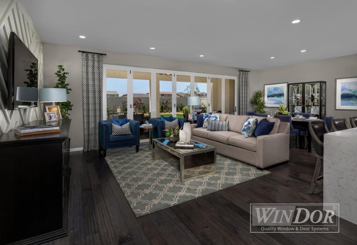 Bright modern living room with beige sofa, blue chairs, coffee table, and large windows.
