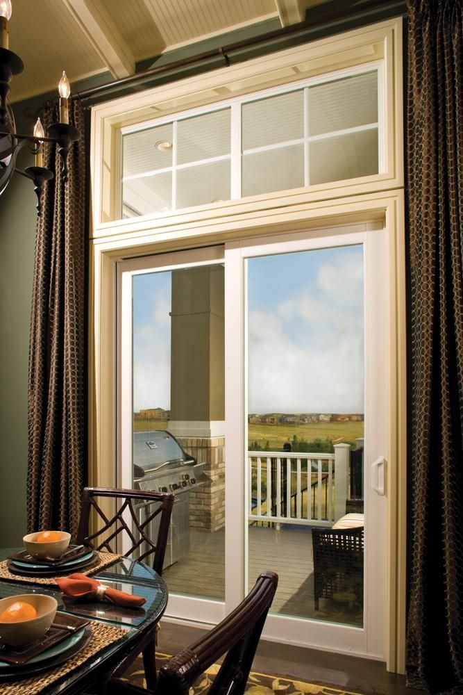 Dining table by an open glass door with a view of a balcony and cloudy sky.