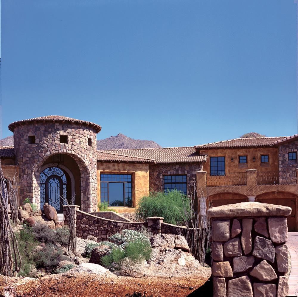 Stone desert house with arched entry, tiled roof, and blue sky