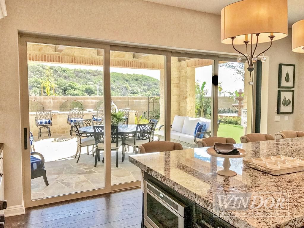 Bright kitchen with granite island opening to a patio through sliding glass doors, with outdoor seating.