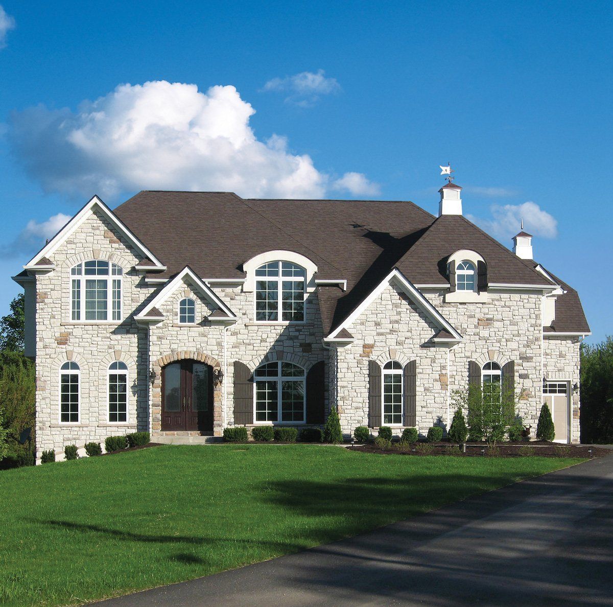 Large stone suburban house with a manicured lawn and blue sky background