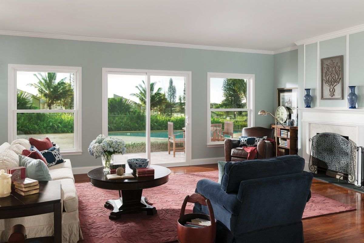 Bright living room with large windows, red rug, blue chairs, and a fireplace overlooking a green garden