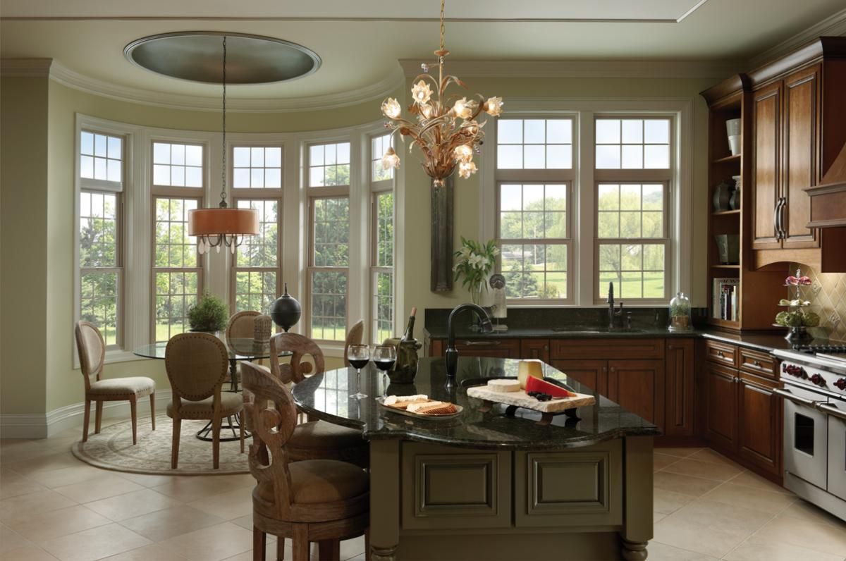 Bright kitchen with large windows, wooden cabinets, island, dining table, and chandelier in a sunlit room