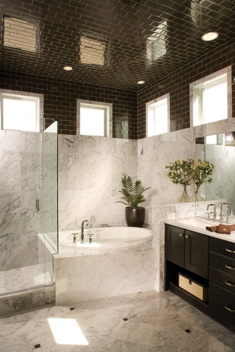 Modern marble bathroom with a freestanding tub, black vanity, and high windows under a dark patterned ceiling