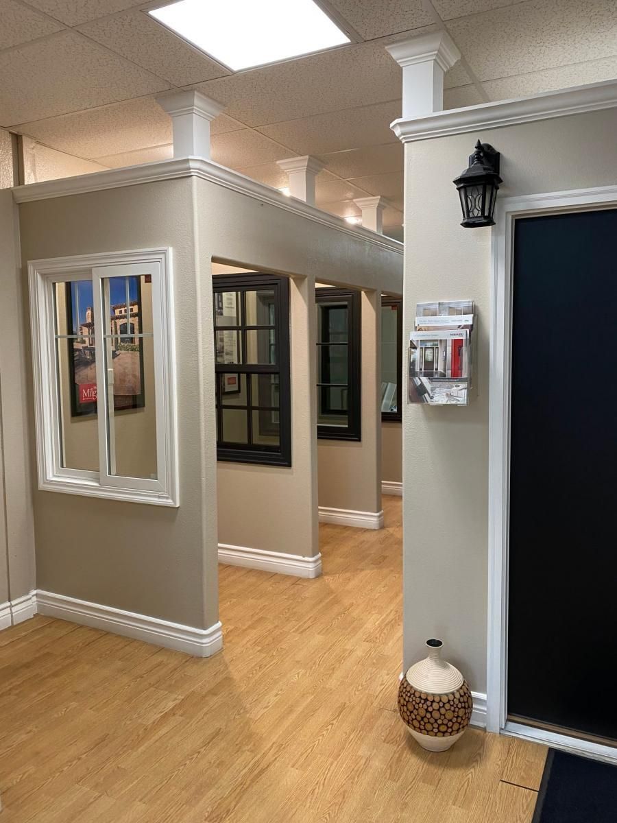 Empty hallway with wood floors, beige walls, mirrors, and black-framed display windows in a bright interior.