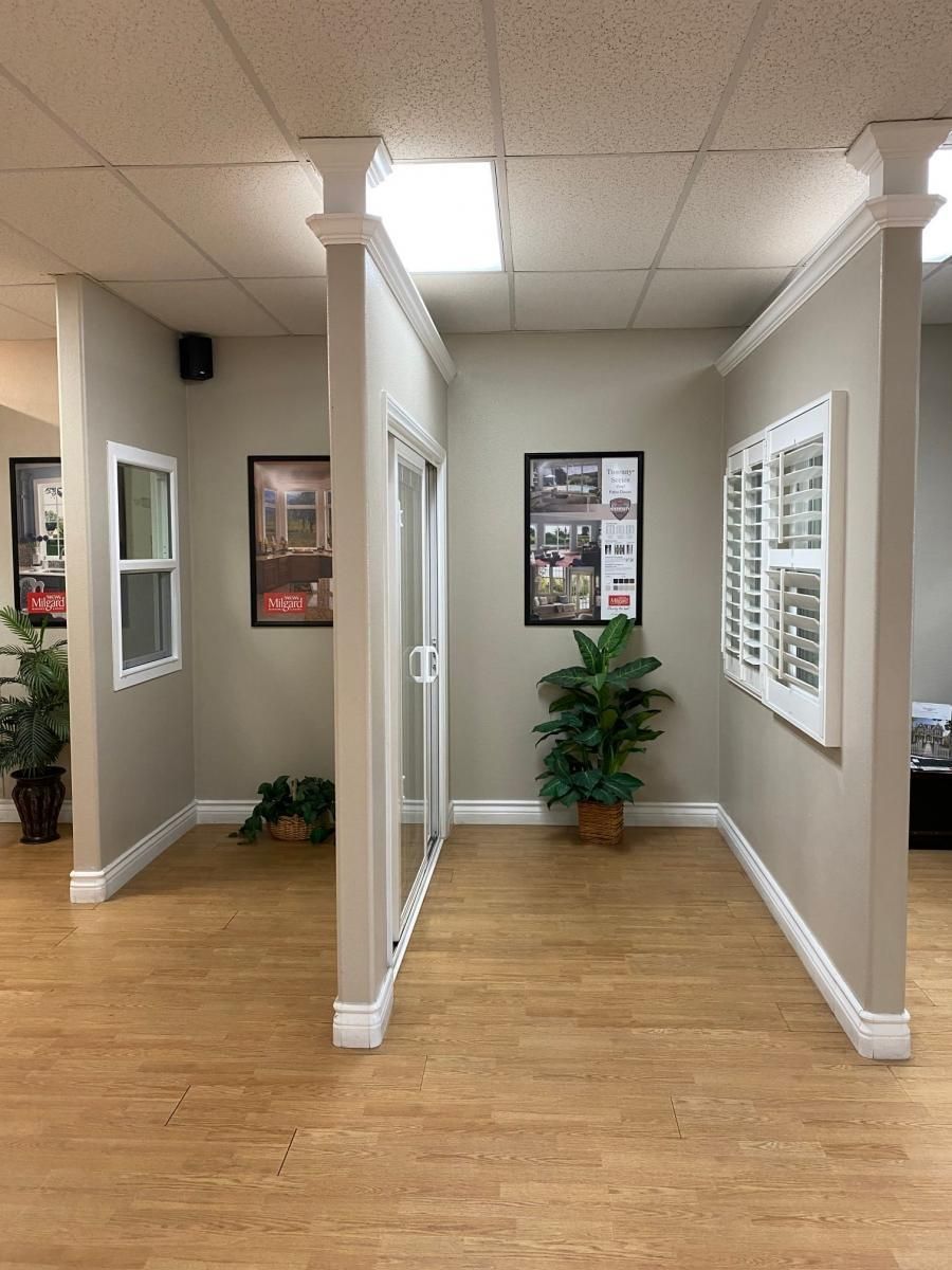 Office hallway with beige walls, wood floor, white trim, and potted plants near framed wall art.