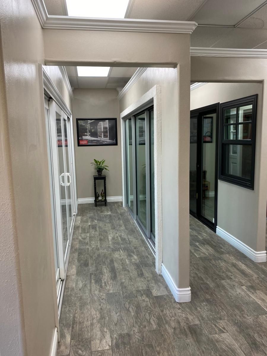 Office hallway with gray carpet, beige walls, glass doors, and a plant at the far end.