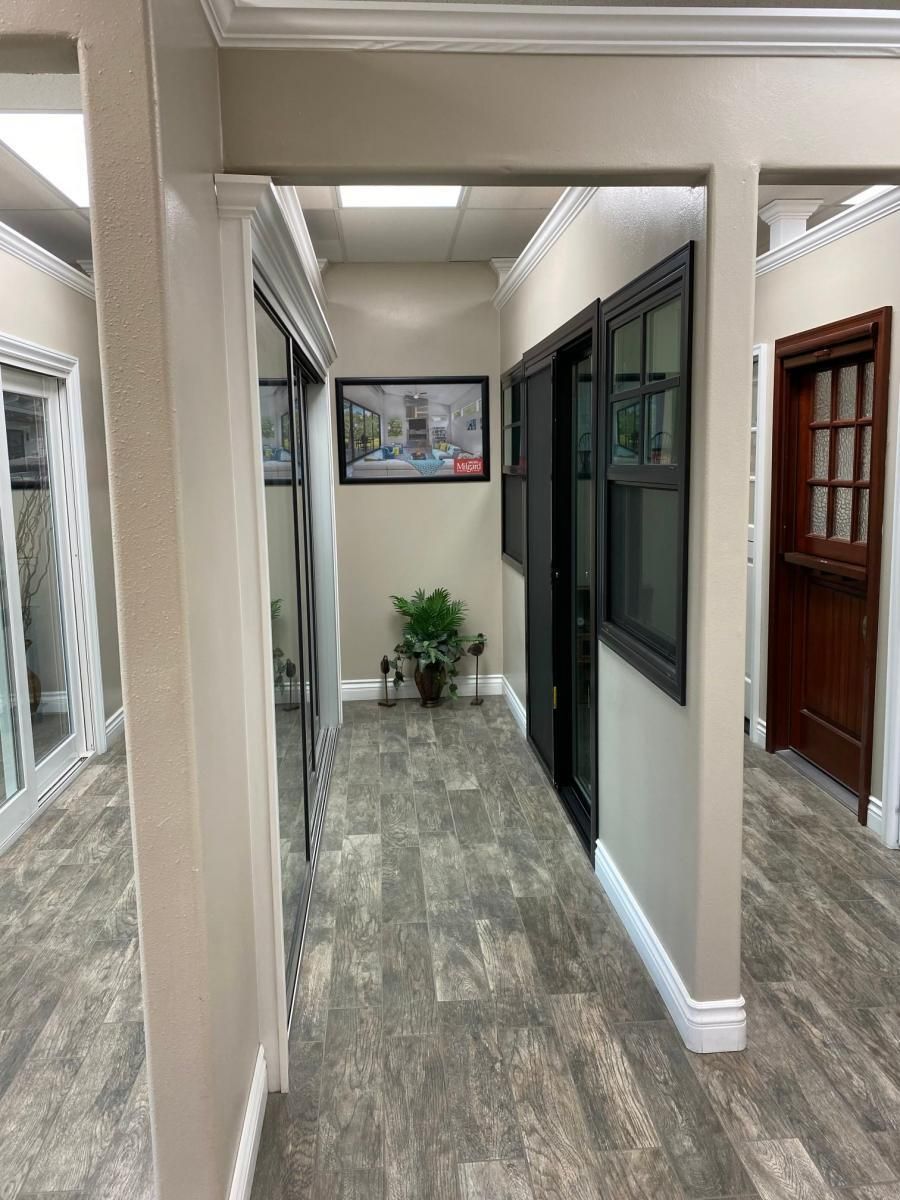 Narrow indoor hallway with tiled floor, windows, doors, and a potted plant at the end.
