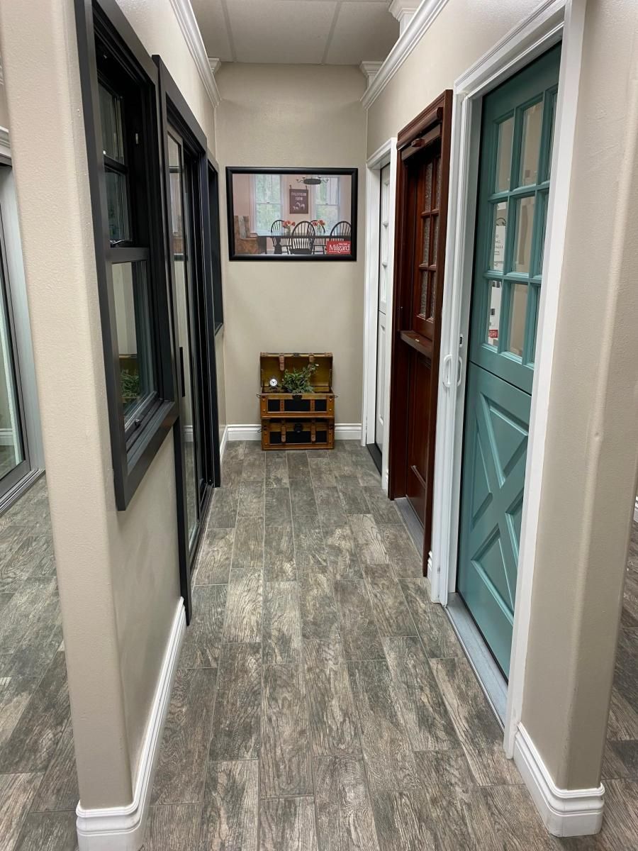 Narrow hallway with multiple doors, gray wood floor, and a framed wall sign at the end.