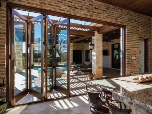 Indoor-outdoor room with open glass doors, brick walls, and sunlight casting shadows on the floor