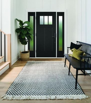 Modern entryway with black front door, potted plant, bench, and striped rug