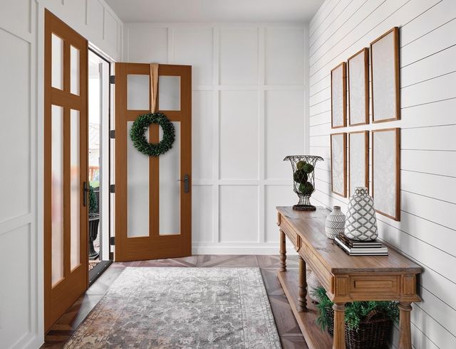 Bright entryway with white walls, wood doors, a wreath, rug, and console table with decor.